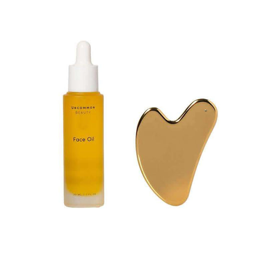 Hydrating Face Oil bottle with stainless steel Gua Sha tool on white background
