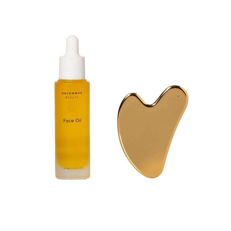 Hydrating Face Oil bottle with stainless steel Gua Sha tool on white background