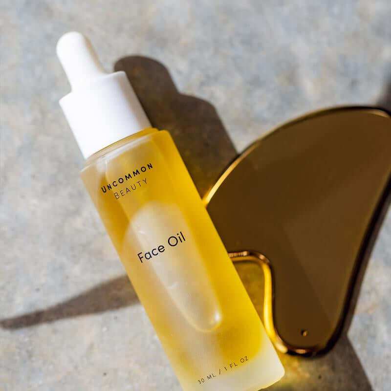 Hydrating face oil bottle with stainless steel gua sha tool on white surface for skincare routine